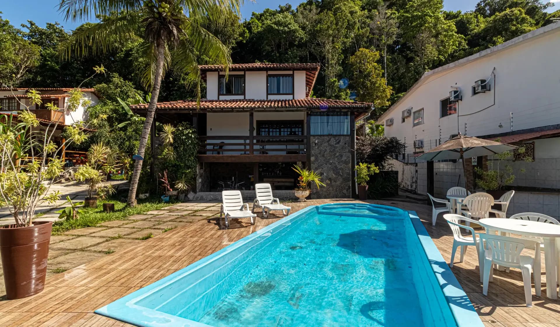 Piscina e deck da Casa 1 com a fachada e os coqueiros ao fundo