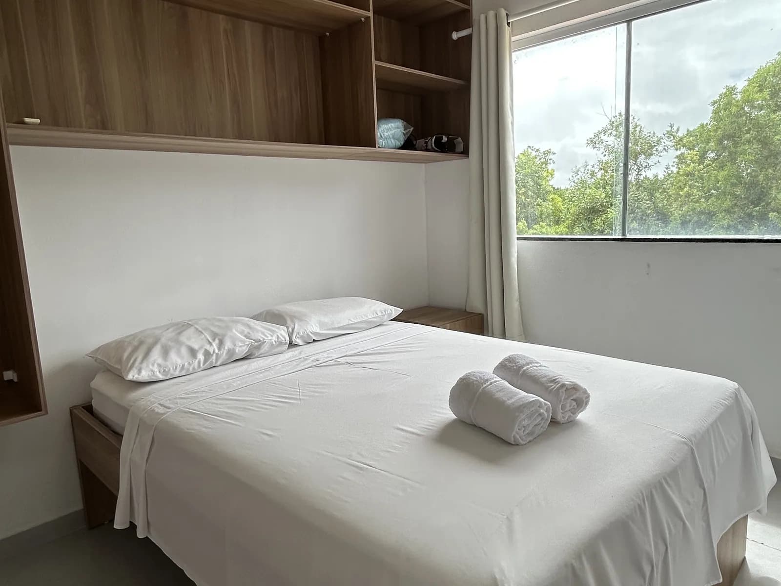 Quarto do apartamento com janela ampla e vista para a vegetação