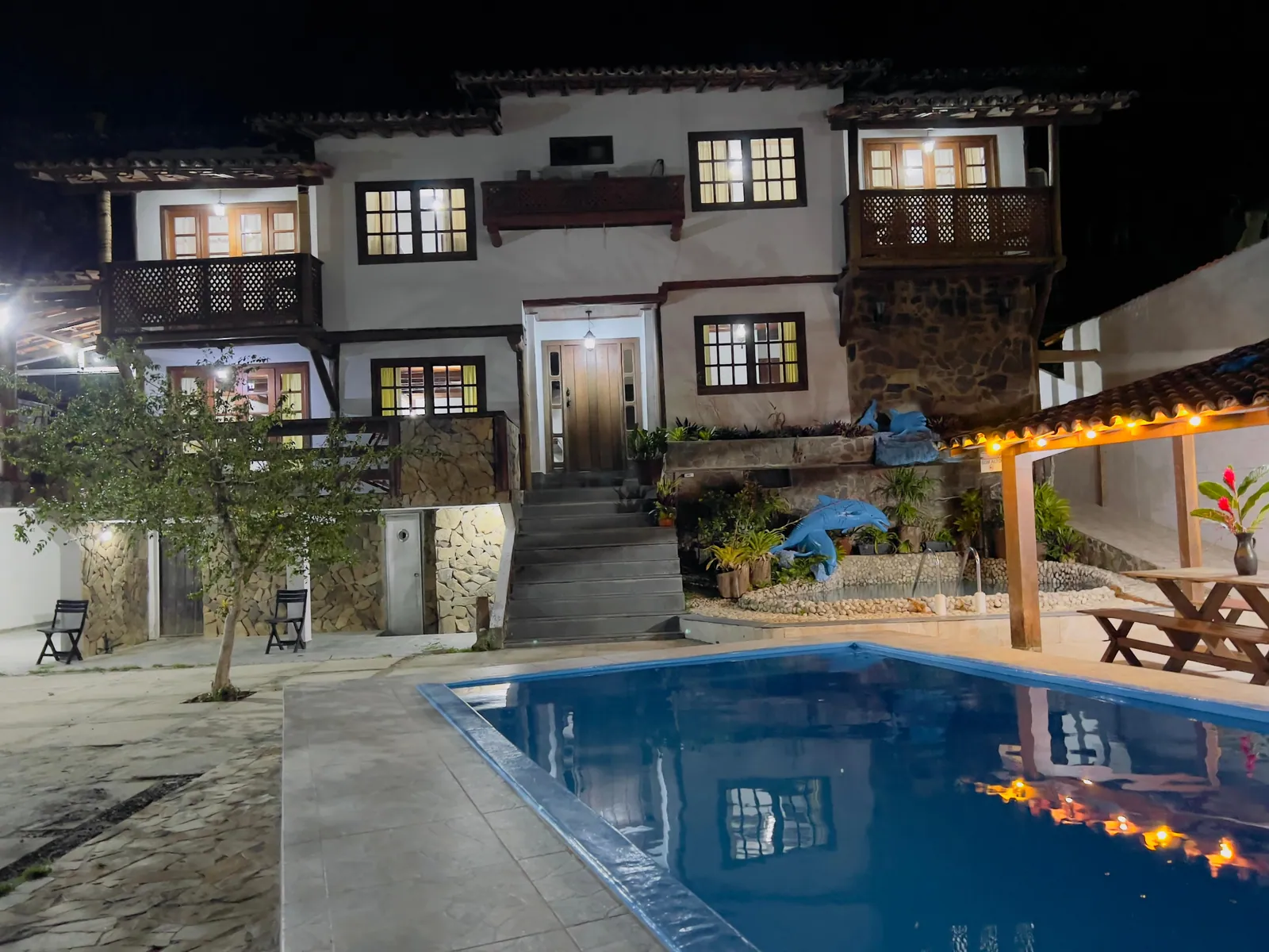 Piscina da Casa 2 iluminada à noite, com a casa ao fundo