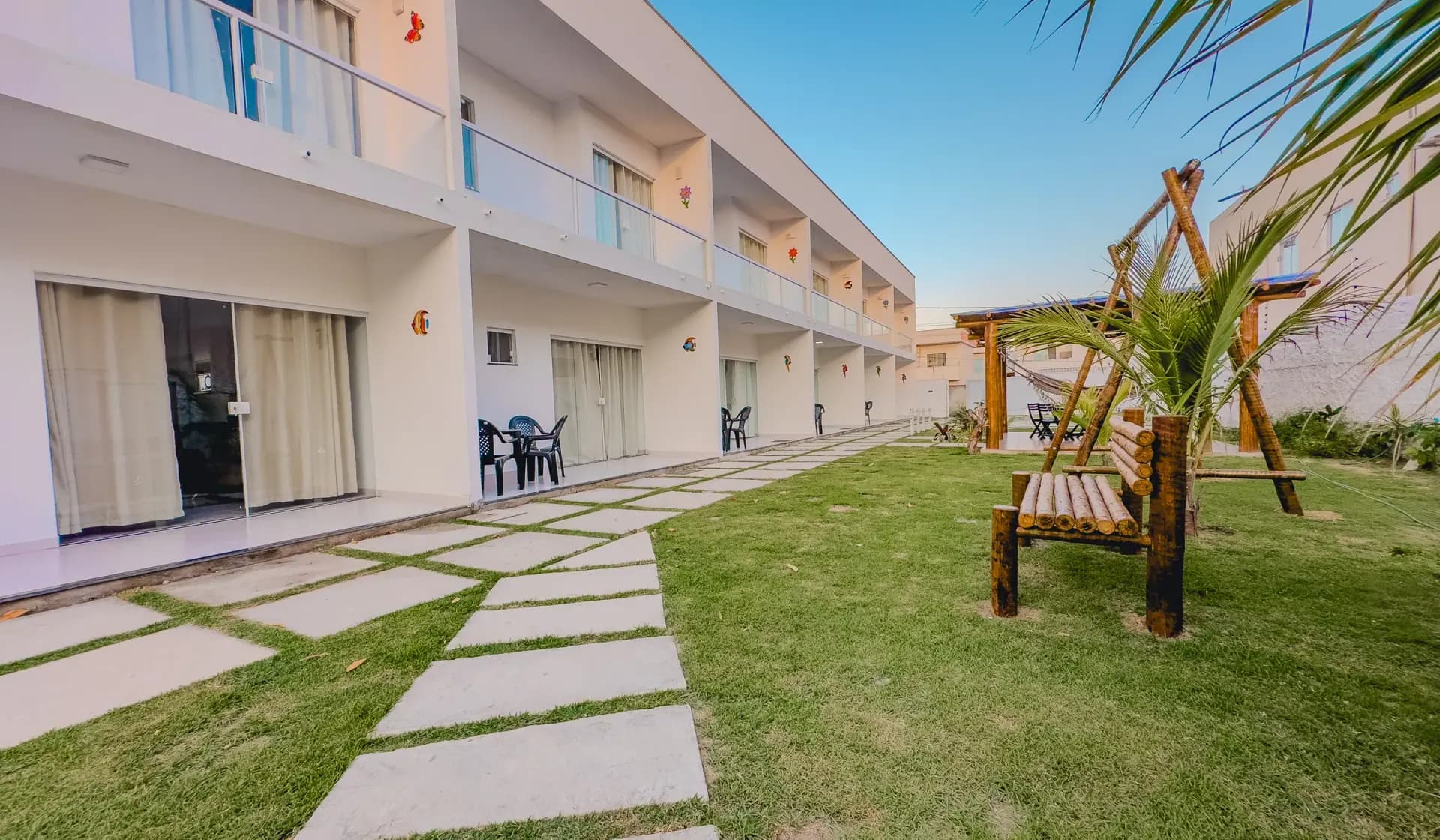 Jardim central do Village Mariah Condomínio ao entardecer, com os apartamentos ao fundo