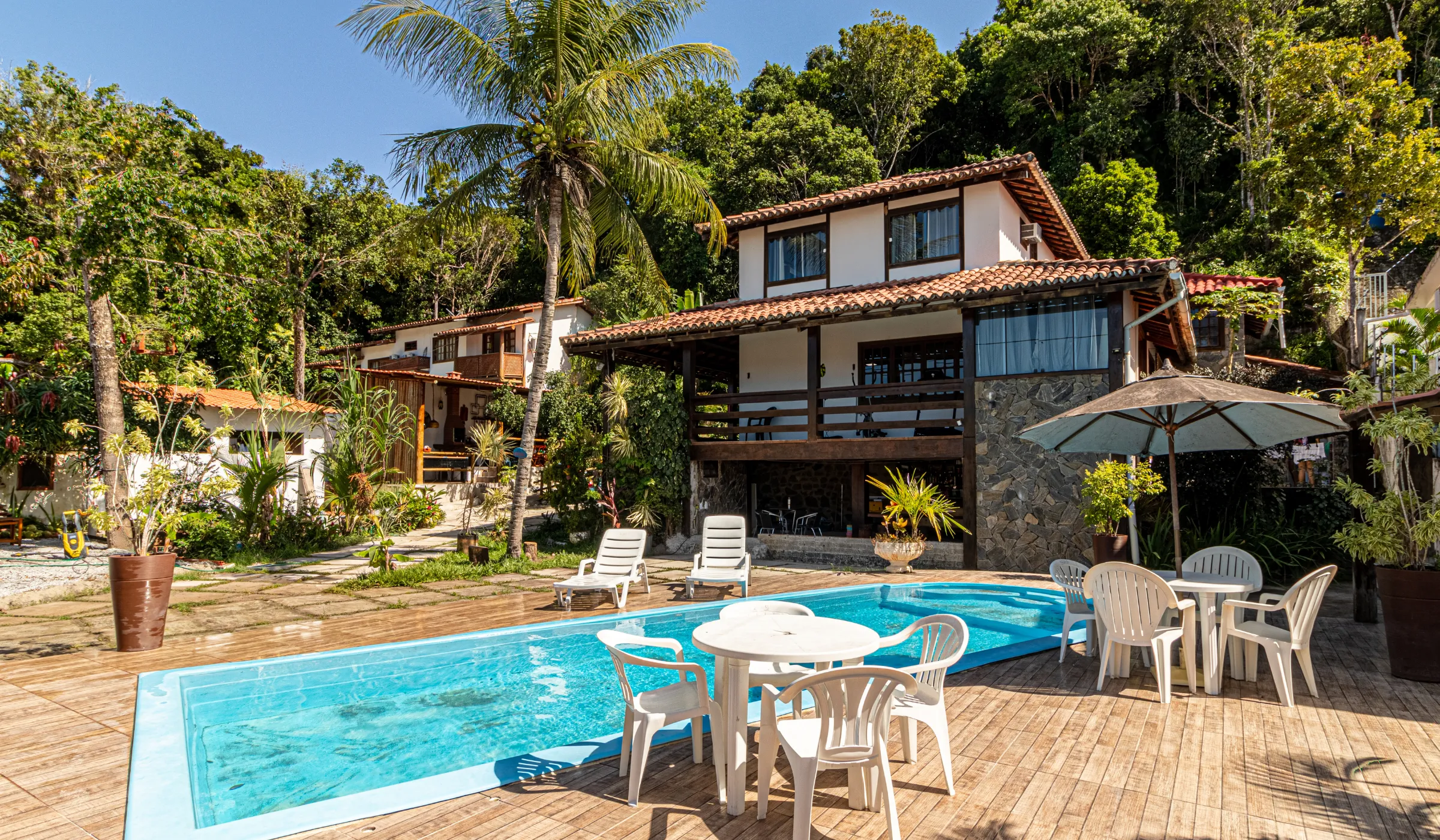 Piscina e deck da Casa 1 com a fachada e os coqueiros ao fundo